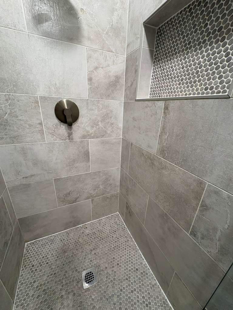 Walk-in tile shower renovation with penny-tile floor and niche
